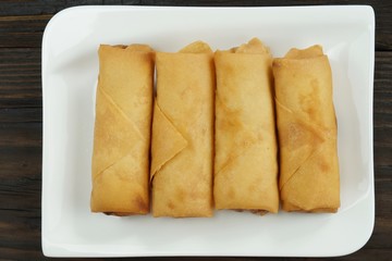 Fried Chinese spring rolls served with chili sauce and decorated rose tomatoes with green leaved on wood, space. Concept Asian food