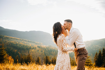 Loving bride kisses his wife, holding her face against the background of mountains and sunset