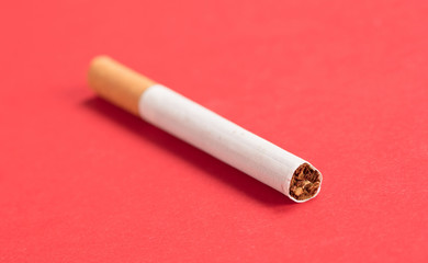 Single cigarette isolated on red background