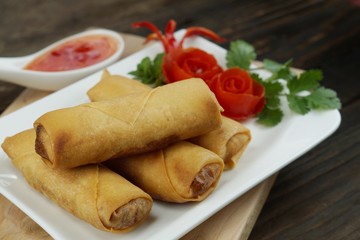Fried Chinese spring rolls served with chili sauce and decorated rose tomatoes with green leaved on wood, space. Concept Asian food