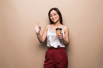 Asian cute girl holding coffee cup with okay sign on beige background