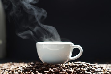 a cup of hot coffee with steaming and beans on wooden and black background
