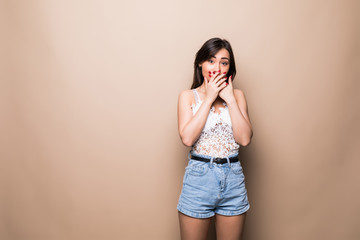 Shocked woman covering her mouth by hand isolated on beige background