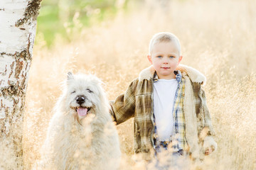 Happy smiling blond boy walking with dog friend on farm