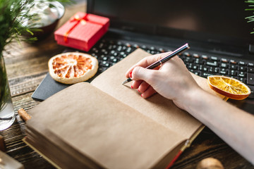Woman's hand is writing in notebook plans and goals on wooden background. Christmas message to yourself in the new year.