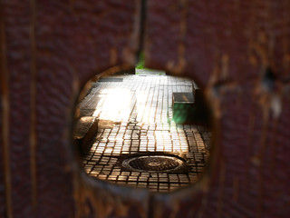 An old wooden door has a hole through which you can peek into the courtyard
