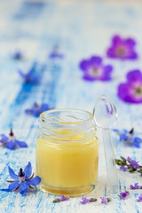 Raw organic royal jelly in a small bottle with litte spoon on small bottle surrounded by flowers.