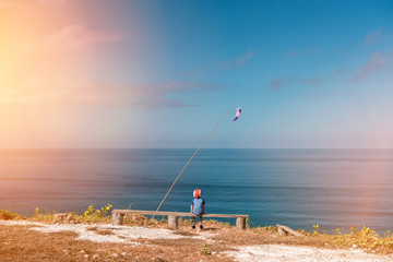 Dreaming boy sits on a bench in a helmet on the background of the sea. View point