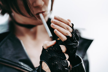 Cool Rock girl in a black leather jacket and gloves lights a cigarette. Smoking. Style