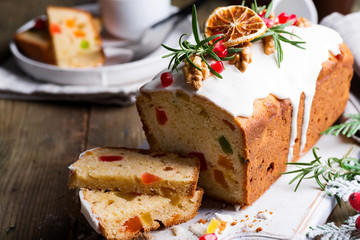 Fruit cake dusted sliced with icing, nuts, kernels pomegranate and dry orange close-up. Christmas...