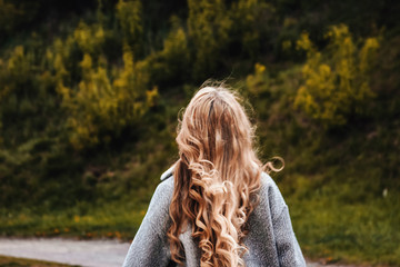 blonde with curly hair stands with her back, hair fluttering in the wind, the girl looks forward...