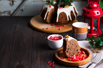 Christmas sliced chocolate cake with white icing and pomegranate kernels on a wooden dark background, cups and decorations,