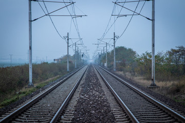 Fototapeta premium Two train tracks leading into distance. Poles with power lines overhead. Very moody and grey atmosphere. Efficient and fast way of transport.