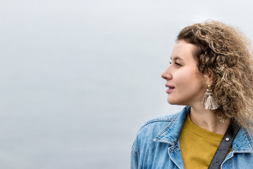Portrait of a young woman with curly hair looking away dreaming, outdoors, profile view.
