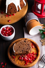 Christmas sliced chocolate cake with white icing and pomegranate kernels on a wooden dark background, flat lay