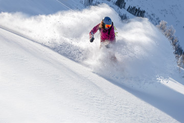 female snowboarder curved and brakes spraying loose deep snow on the freeride slope. downhill with snowboards in fresh snow. freeride world champion. swirls of snow in the air, in a bright mask