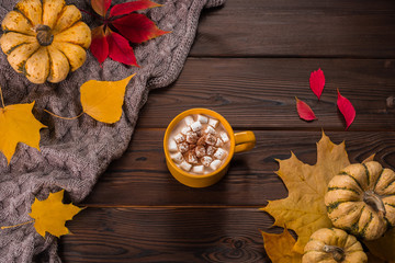 Autumn flat lay. Pumpkins and yellow leaves on knitted plaid. Wooden background. Yellow cup with coffee and marshmallow.