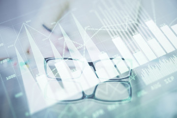 Hand taking notes in notepad. Forex chart holograms in front. Concept of research. Double exposure