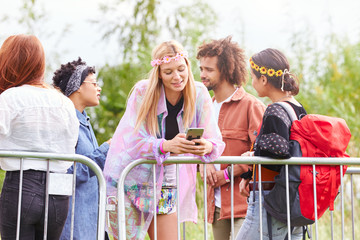 Young Woman Looking At Mobile Phone As She Waits Behind Barrier At Entrance To Music Festival Site
