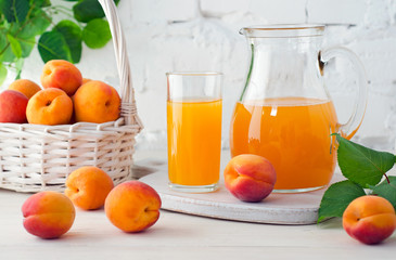 Glass and carafe with apricot juice and apricot fruits in basket on light background