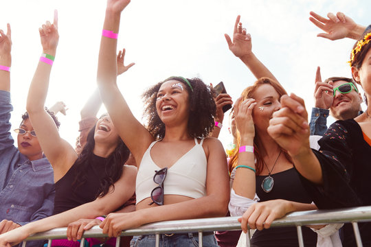 Young Friends In Audience Behind Barrier Dancing And Singing At Outdoor Festival Enjoying Music