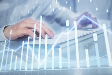 Double exposure of graph with man typing on computer in office on background. Concept of hard work. Closeup.