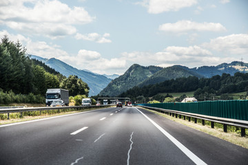 Autobahn or highway with a bridge in the mountains with clear marking surrounded by vibrant green trees under blue sky. Mountain in the background. The Alps, Austria