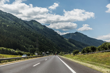 Autobahn or highway with a bridge in the mountains with clear marking surrounded by vibrant green trees under blue sky. Mountain in the background. The Alps, Austria