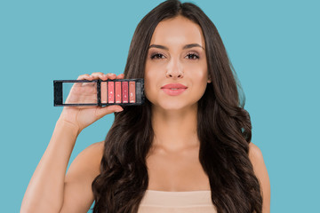 Naklejka premium beautiful woman holding lip gloss palette isolated on blue