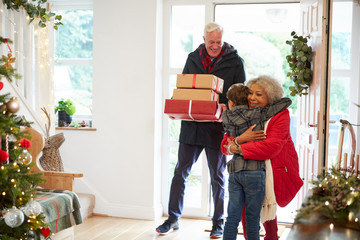 Excited Grandson Greeting Grandparents With Presents Visiting On Christmas Day