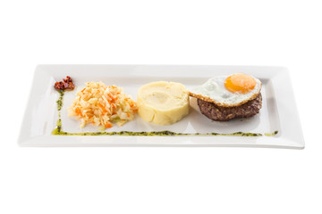 Fried egg with beefsteak, mashed potatoes and pickled cabbage on white plate isolated on white background
