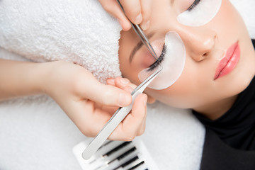 Eyelash extension procedure. Master tweezers fake long lashes beautiful female eyes - obrazy, fototapety, plakaty