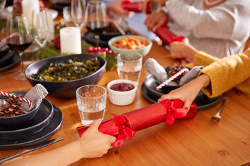 Close Up Of Multi Generation Family Pulling Christmas Crackers As They Sit For Meal At Table