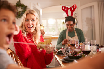 Multi Generation Family Opening Christmas Crackers As They Sit For Meal At Table