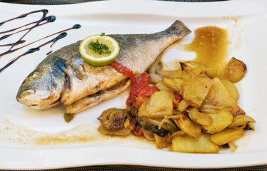 Sea bream fish with potato on white plate close-up