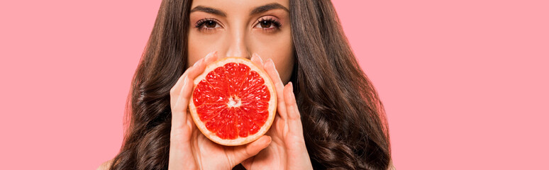 panoramic shot of woman in swimsuit covering face with half of grapefruit isolated on pink