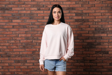 Portrait of young woman in sweater at brick wall. Mock up for design