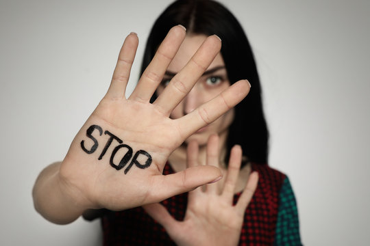 Young woman with word STOP written on her palm against light background, focus on hand