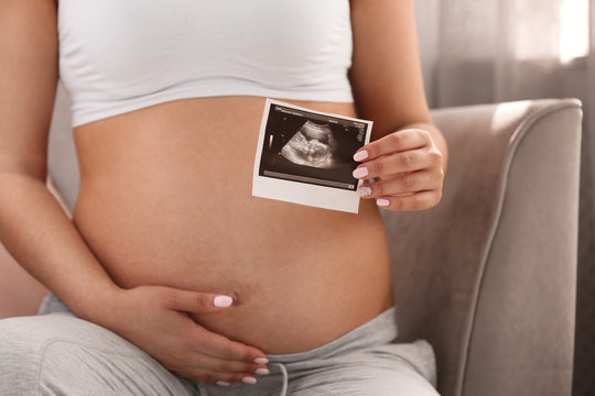 Pregnant woman with ultrasound picture at home, closeup
