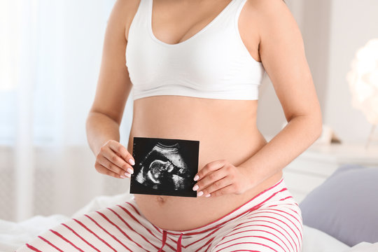Pregnant woman with ultrasound picture on bed, closeup