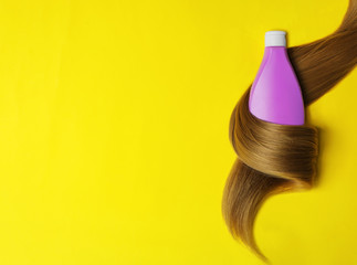 Shampoo bottle wrapped in lock of hair on yellow background, flat lay with space for text. Natural cosmetic products