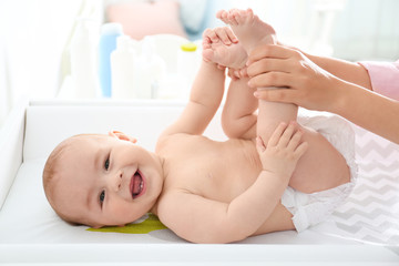 Young woman massaging cute baby on changing table