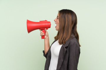 Young brunette girl with blazer over isolated green background shouting through a megaphone