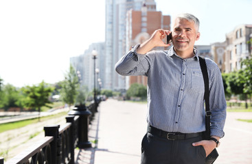 Handsome businessman talking by mobile phone in city, space for text