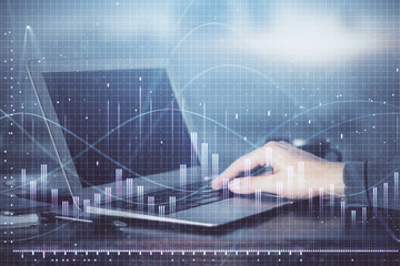 Double exposure of businessman's hands with laptop and stock market graph background. Concept of research and trading.