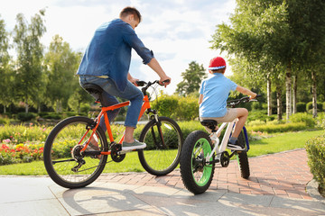 Fototapeta premium Dad and son riding modern bicycles outdoors