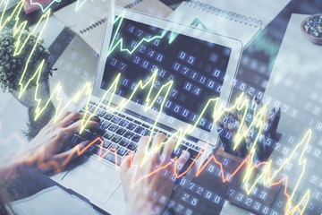 Double exposure of businessman's hands with laptop and stock market graph background. Concept of research and trading.