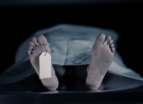 Cadaver on autopsy table at morgue, label tied to toe, close-up
