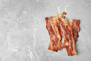 Slices of tasty fried bacon on light grey marble table, top view. Space for text