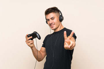 Young handsome man playing with a video game controller over isolated background smiling and showing victory sign